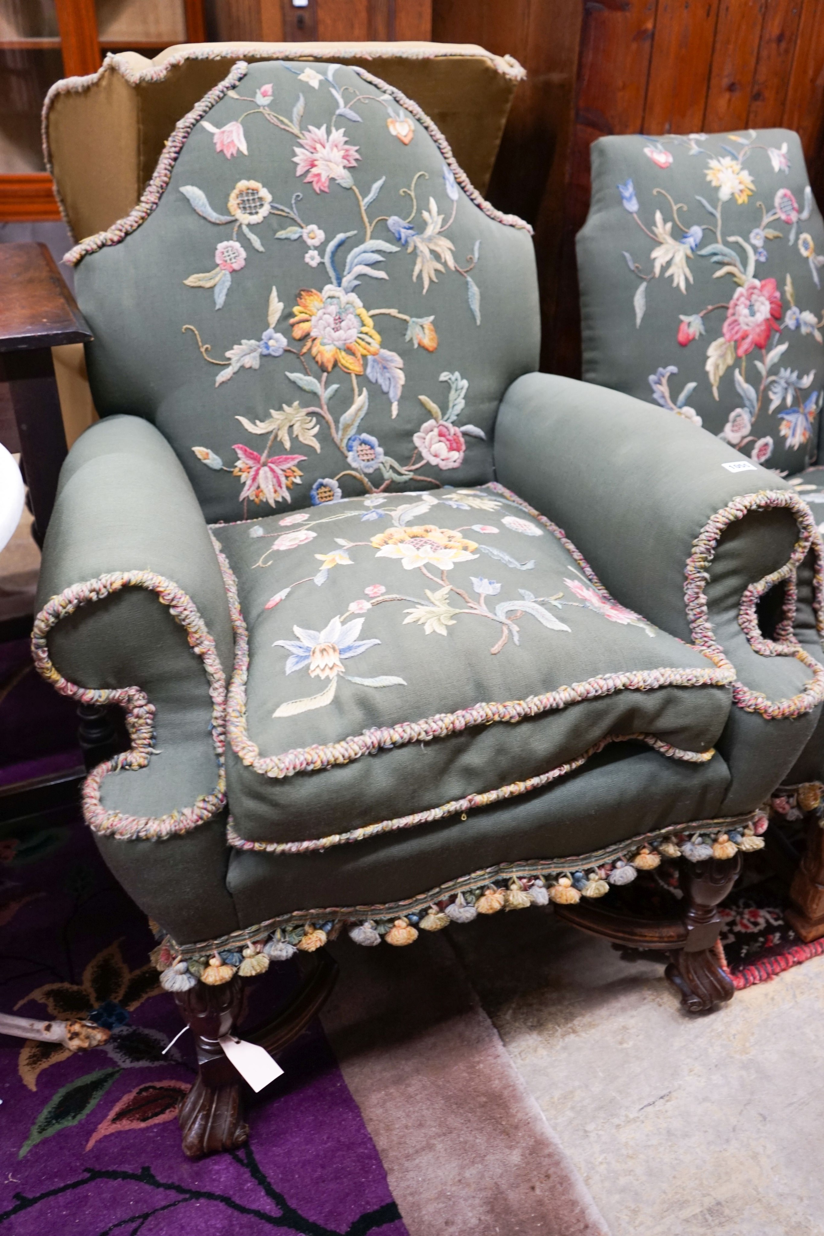 Two armchairs with shaped backs, each upholstered in green with embroidered flowers, on shaped cross stretchers with scrolled feet, larger width 80cm, depth 70cm, height 102cm
